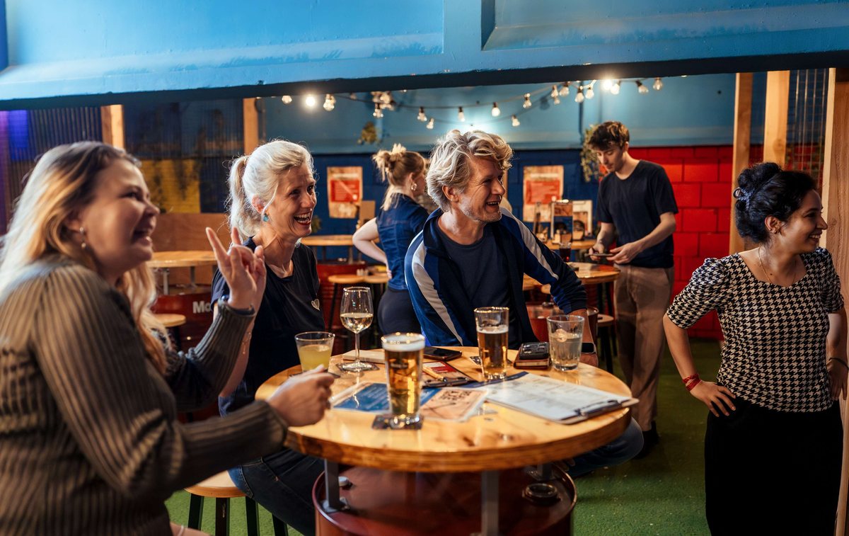 Collega's lachen aan een statafel naast de axe throwing banen